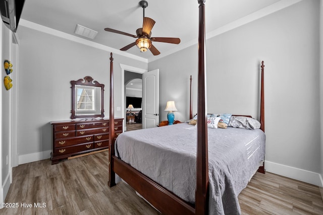 bedroom with wood finished floors, arched walkways, baseboards, and visible vents