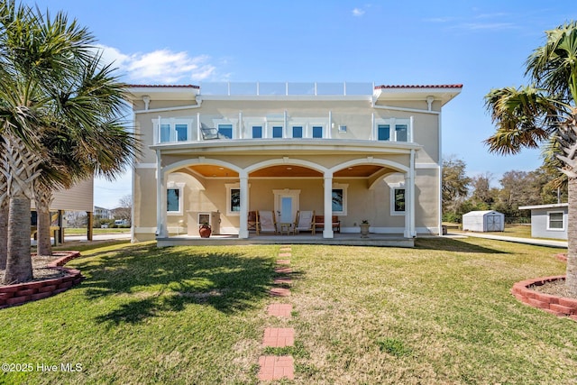 back of house featuring an outdoor structure, a shed, stucco siding, a balcony, and a yard