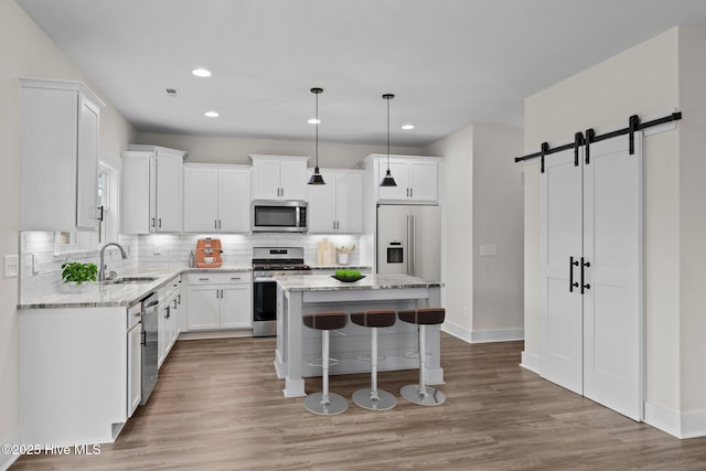 kitchen featuring a breakfast bar, stainless steel appliances, backsplash, a barn door, and a sink