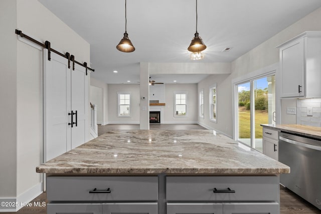 kitchen with decorative backsplash, stainless steel dishwasher, a barn door, ceiling fan, and light stone countertops