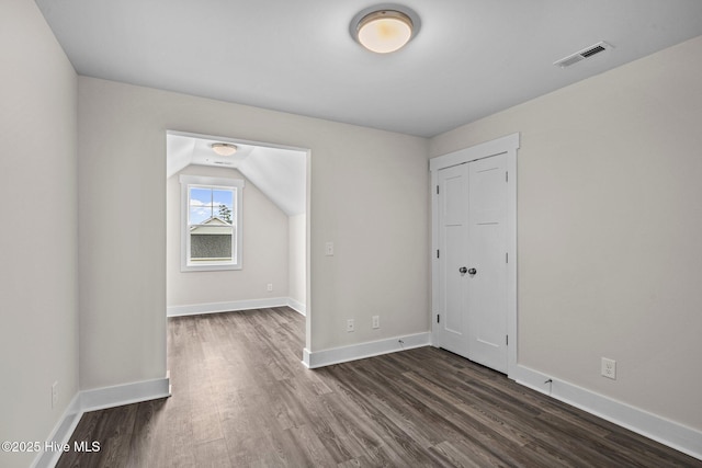 empty room featuring lofted ceiling, baseboards, visible vents, and dark wood finished floors