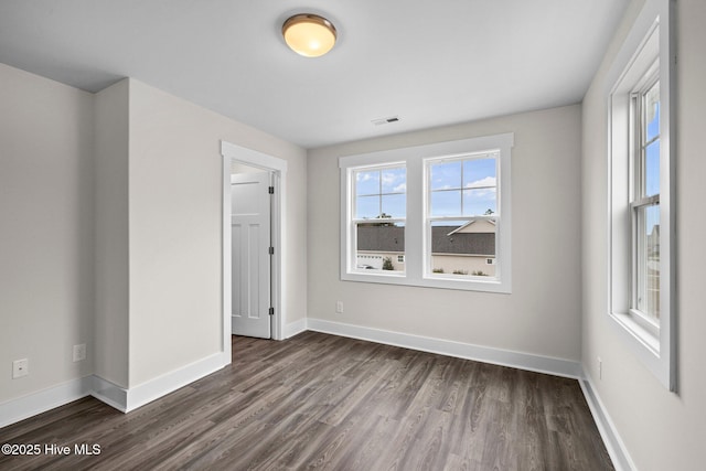 unfurnished room featuring dark wood-type flooring, visible vents, and baseboards