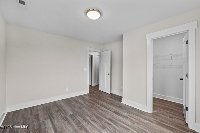 unfurnished bedroom with a walk in closet, visible vents, baseboards, and wood finished floors