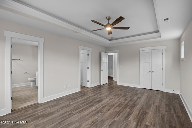 unfurnished bedroom with a closet, a raised ceiling, dark wood finished floors, and baseboards