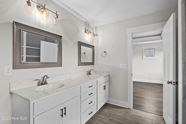 full bath featuring double vanity, wood finished floors, a sink, and baseboards