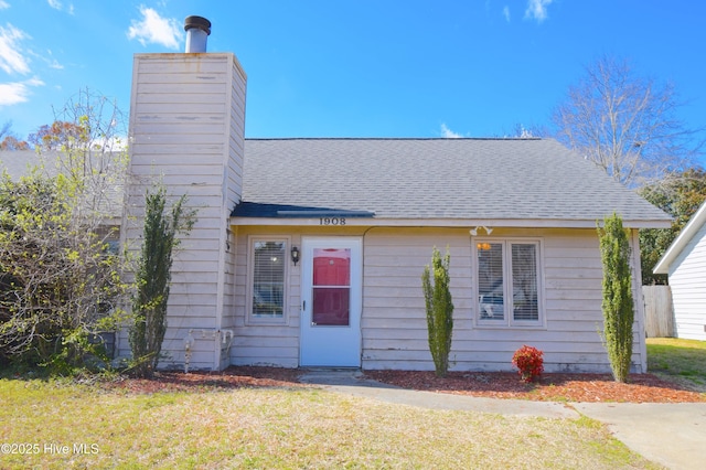 view of front of property with roof with shingles, a chimney, and a front lawn