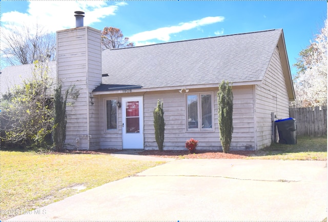 view of front of property featuring roof with shingles, a front lawn, a chimney, and fence