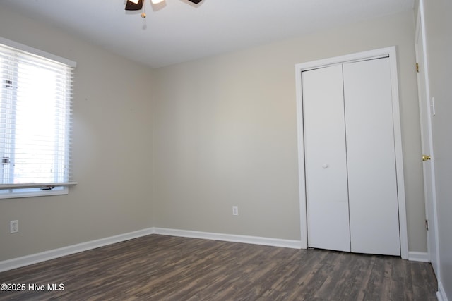 unfurnished bedroom featuring dark wood-type flooring, a closet, baseboards, and a ceiling fan