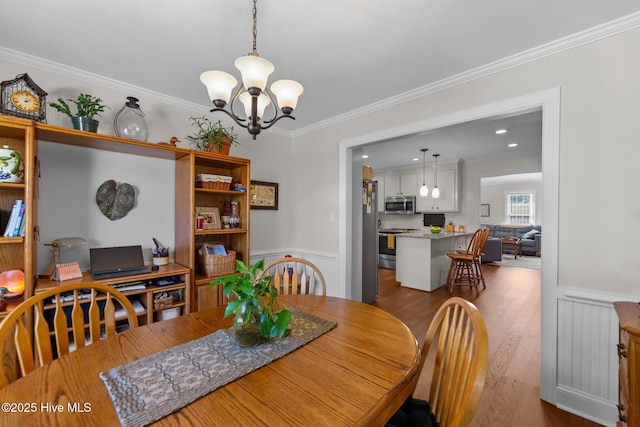 dining space featuring ornamental molding, wainscoting, a notable chandelier, and wood finished floors