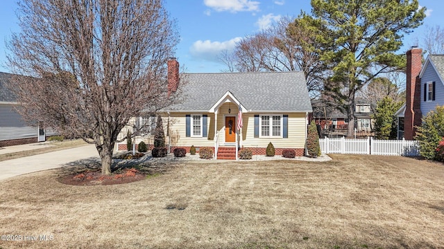 view of front of property with roof with shingles, a chimney, concrete driveway, a front yard, and fence