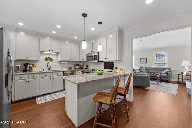 kitchen featuring a peninsula, stainless steel appliances, a sink, and wood finished floors