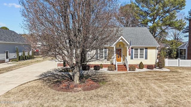 view of property hidden behind natural elements with driveway, a front yard, fence, and roof with shingles