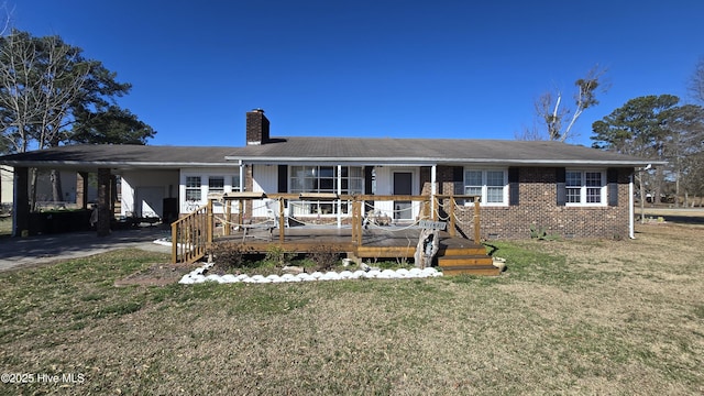 ranch-style house featuring brick siding, a chimney, an attached carport, driveway, and a front lawn