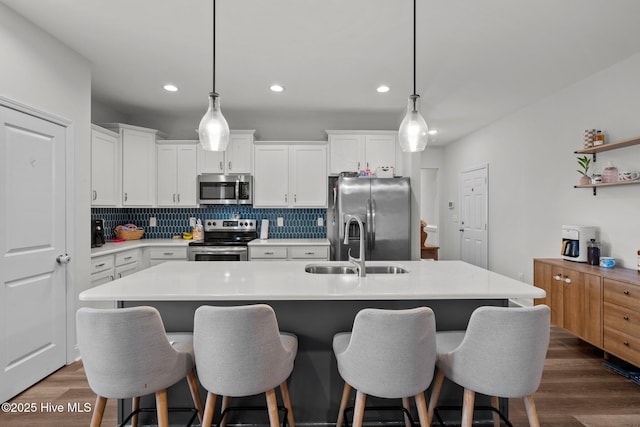 kitchen featuring stainless steel appliances, a sink, white cabinets, decorative backsplash, and dark wood-style floors