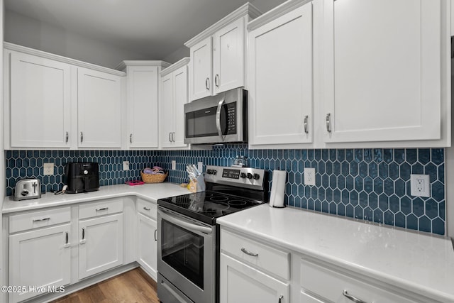 kitchen featuring white cabinets, appliances with stainless steel finishes, wood finished floors, light countertops, and backsplash