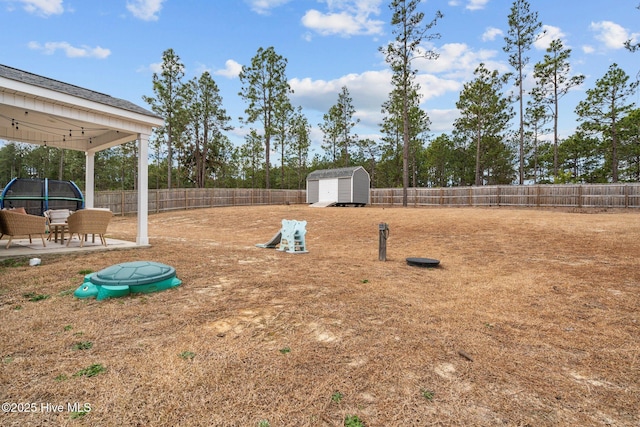 view of yard with a trampoline, a fenced backyard, an outdoor structure, and a storage shed