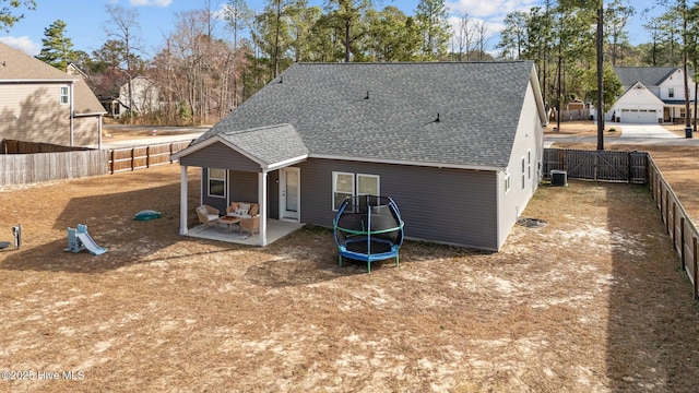 rear view of house featuring central AC unit, a patio, a fenced backyard, roof with shingles, and a trampoline