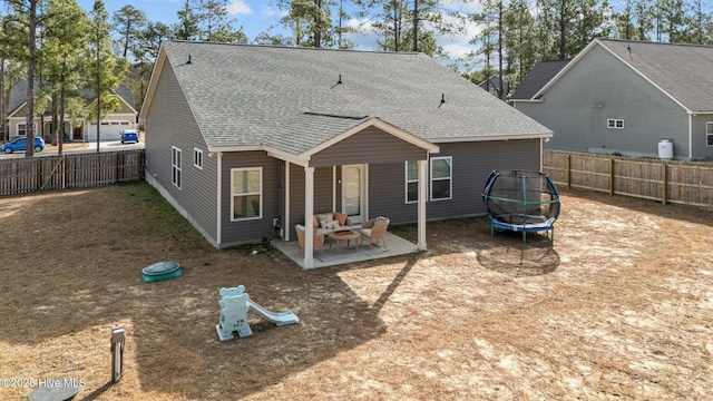 back of property with a shingled roof, a trampoline, a patio area, and a fenced backyard