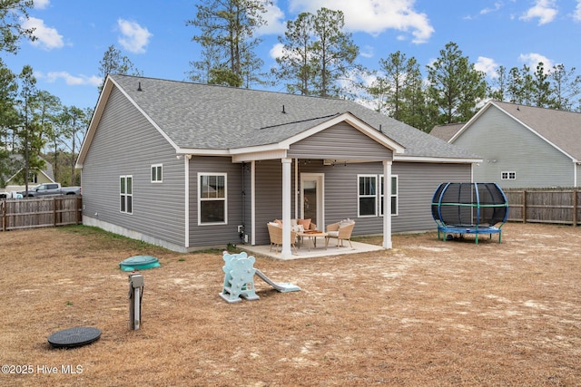 back of property featuring a shingled roof, a trampoline, a patio area, and a fenced backyard