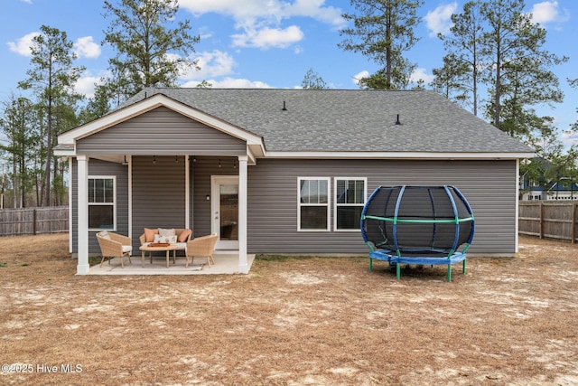 rear view of property featuring a patio, roof with shingles, a trampoline, fence, and an outdoor living space