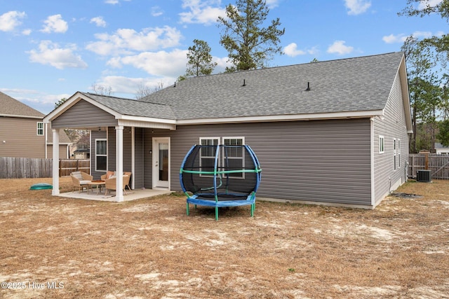 rear view of house featuring a patio, central AC, a shingled roof, fence, and a trampoline