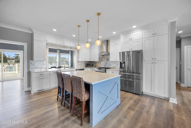 kitchen featuring a sink, white cabinetry, ornamental molding, appliances with stainless steel finishes, and wall chimney exhaust hood