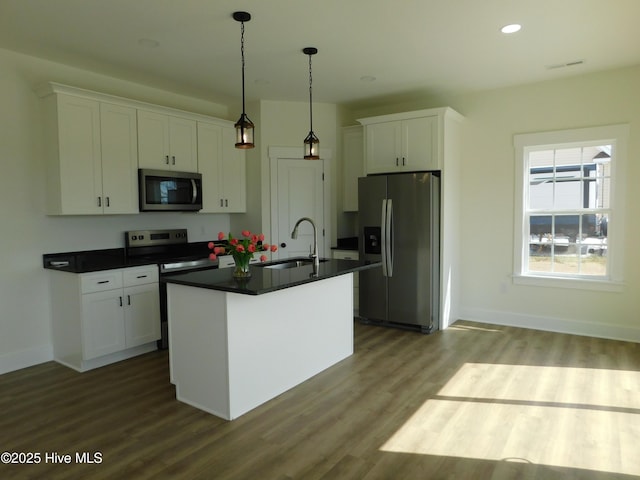 kitchen featuring appliances with stainless steel finishes, dark countertops, a sink, and white cabinetry