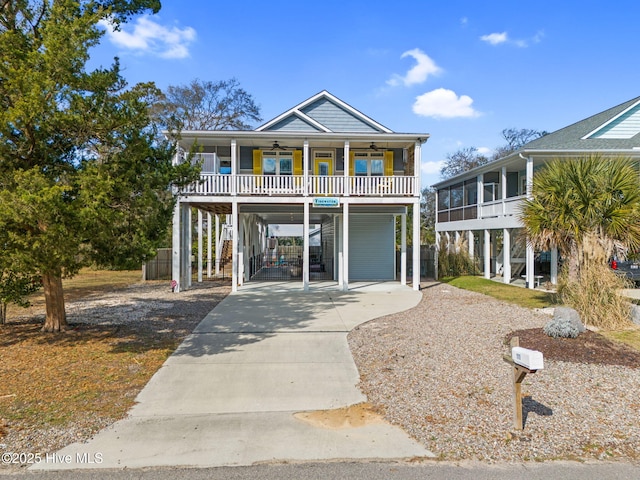 raised beach house with a porch, a ceiling fan, a sunroom, a carport, and driveway