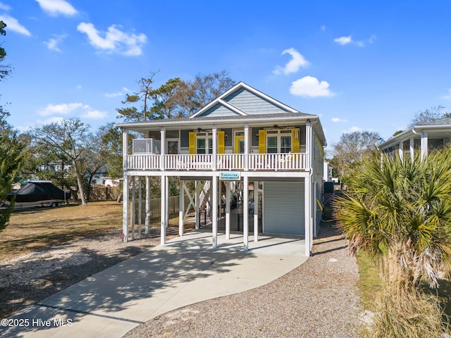 raised beach house featuring a porch, concrete driveway, ceiling fan, a carport, and stairs