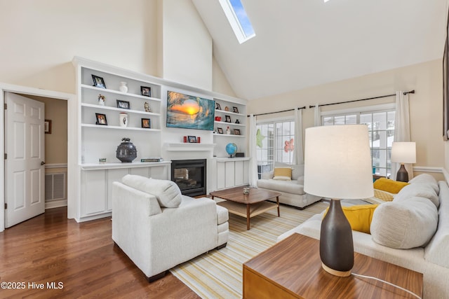 living area with visible vents, a skylight, wood finished floors, a glass covered fireplace, and high vaulted ceiling