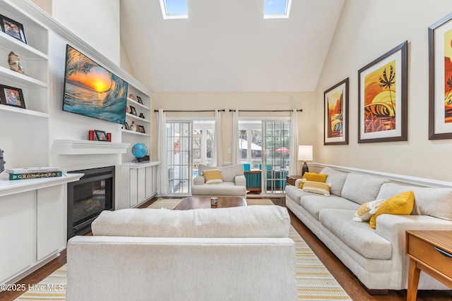 living area featuring high vaulted ceiling, built in features, a glass covered fireplace, wood finished floors, and a skylight