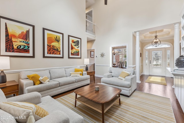 living area featuring decorative columns, wood finished floors, a towering ceiling, and a chandelier