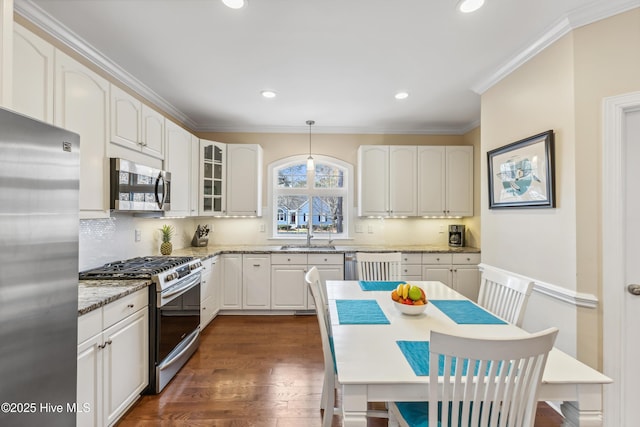 kitchen featuring backsplash, ornamental molding, light stone counters, appliances with stainless steel finishes, and dark wood-style flooring