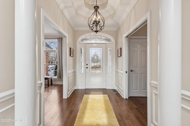 entryway with dark wood-type flooring, a notable chandelier, ornamental molding, wainscoting, and a decorative wall