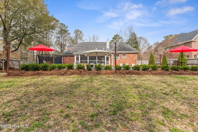 back of property featuring a yard, fence, brick siding, and a chimney