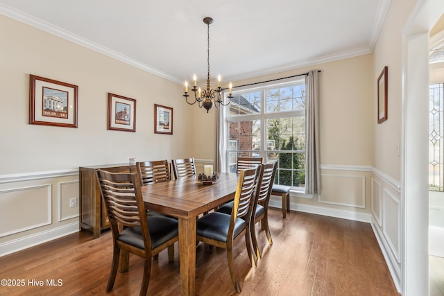 dining room with crown molding, a chandelier, wainscoting, wood finished floors, and a decorative wall