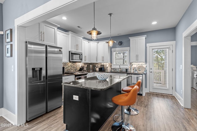 kitchen featuring appliances with stainless steel finishes, a kitchen island, light wood-style flooring, and tasteful backsplash