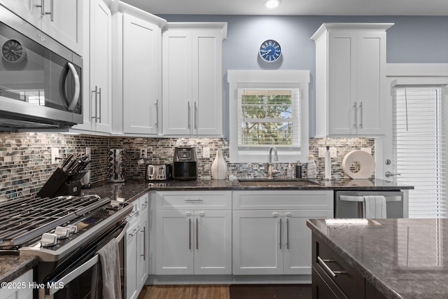 kitchen with stainless steel appliances, dark stone countertops, a sink, and white cabinetry