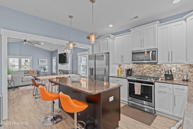 kitchen with a center island, visible vents, backsplash, light wood-style flooring, and appliances with stainless steel finishes