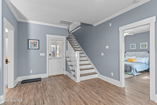 entrance foyer with stairway, crown molding, visible vents, and wood finished floors