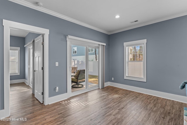 empty room featuring baseboards, visible vents, wood finished floors, and ornamental molding