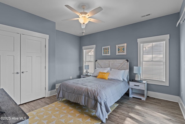 bedroom with a closet, visible vents, ceiling fan, wood finished floors, and baseboards