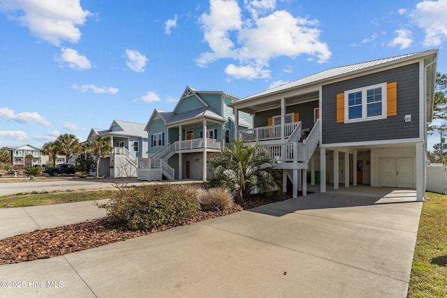 raised beach house featuring metal roof, covered porch, stairs, driveway, and a residential view