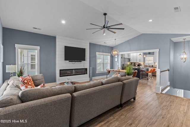 living area with lofted ceiling, visible vents, a fireplace, and wood finished floors