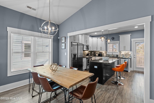 dining room with baseboards, visible vents, lofted ceiling, wood finished floors, and a chandelier