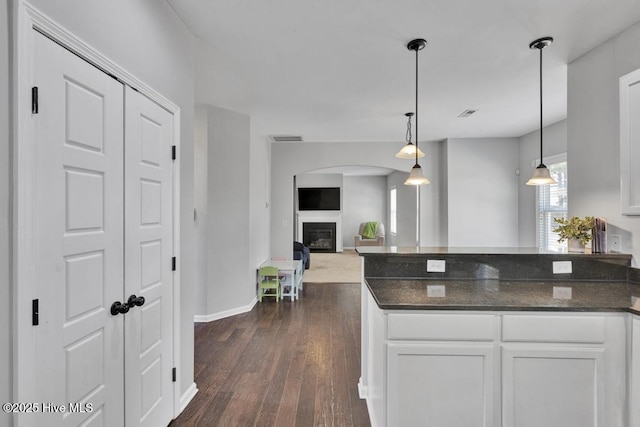 kitchen featuring a peninsula, dark wood finished floors, white cabinets, a glass covered fireplace, and pendant lighting