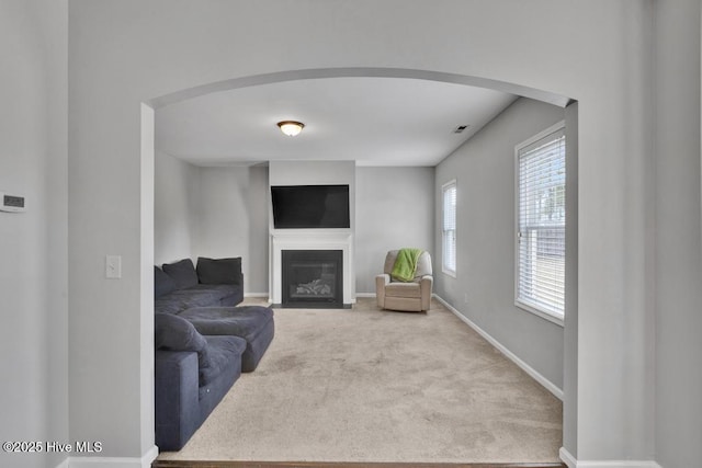 living area with carpet floors, arched walkways, baseboards, and a fireplace with flush hearth