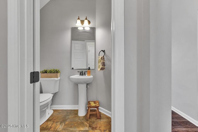 half bath featuring toilet, baseboards, and a sink