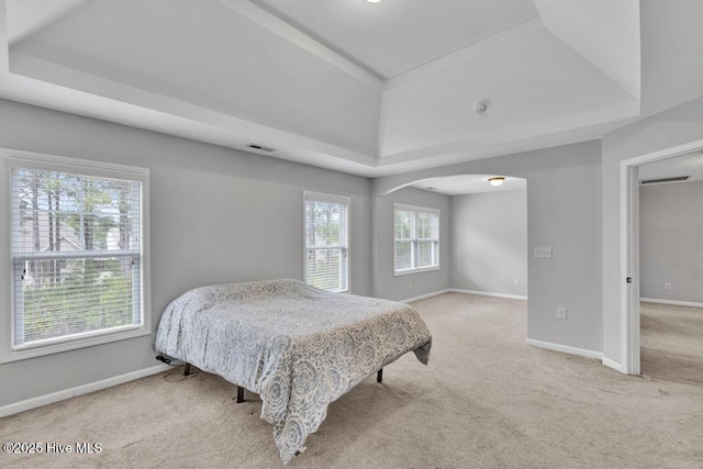 carpeted bedroom with visible vents, baseboards, a raised ceiling, and arched walkways