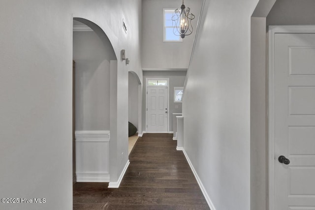 hallway with baseboards, visible vents, arched walkways, wood finished floors, and a high ceiling